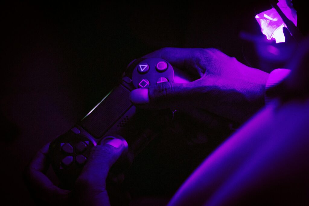 A close-up shot of hands gripping a gaming controller, illuminated by purple light, creating a vibrant atmosphere.