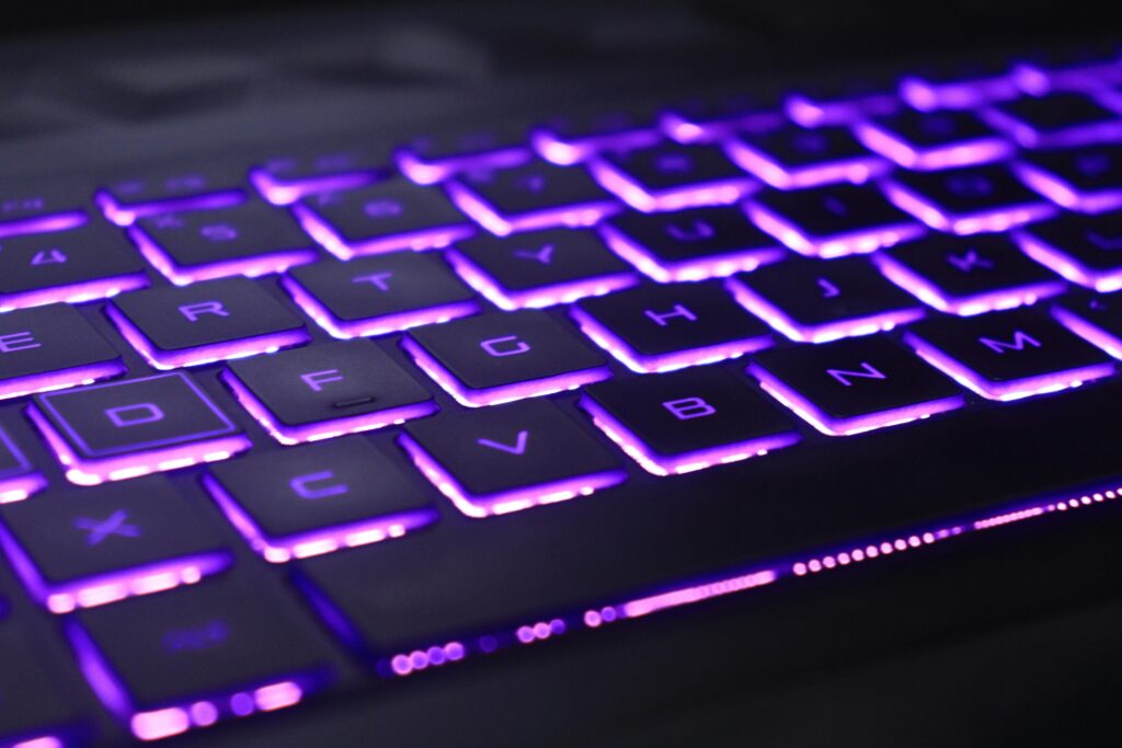 Close-up of a laptop keyboard glowing with vibrant purple neon lights, creating a futuristic tech vibe.