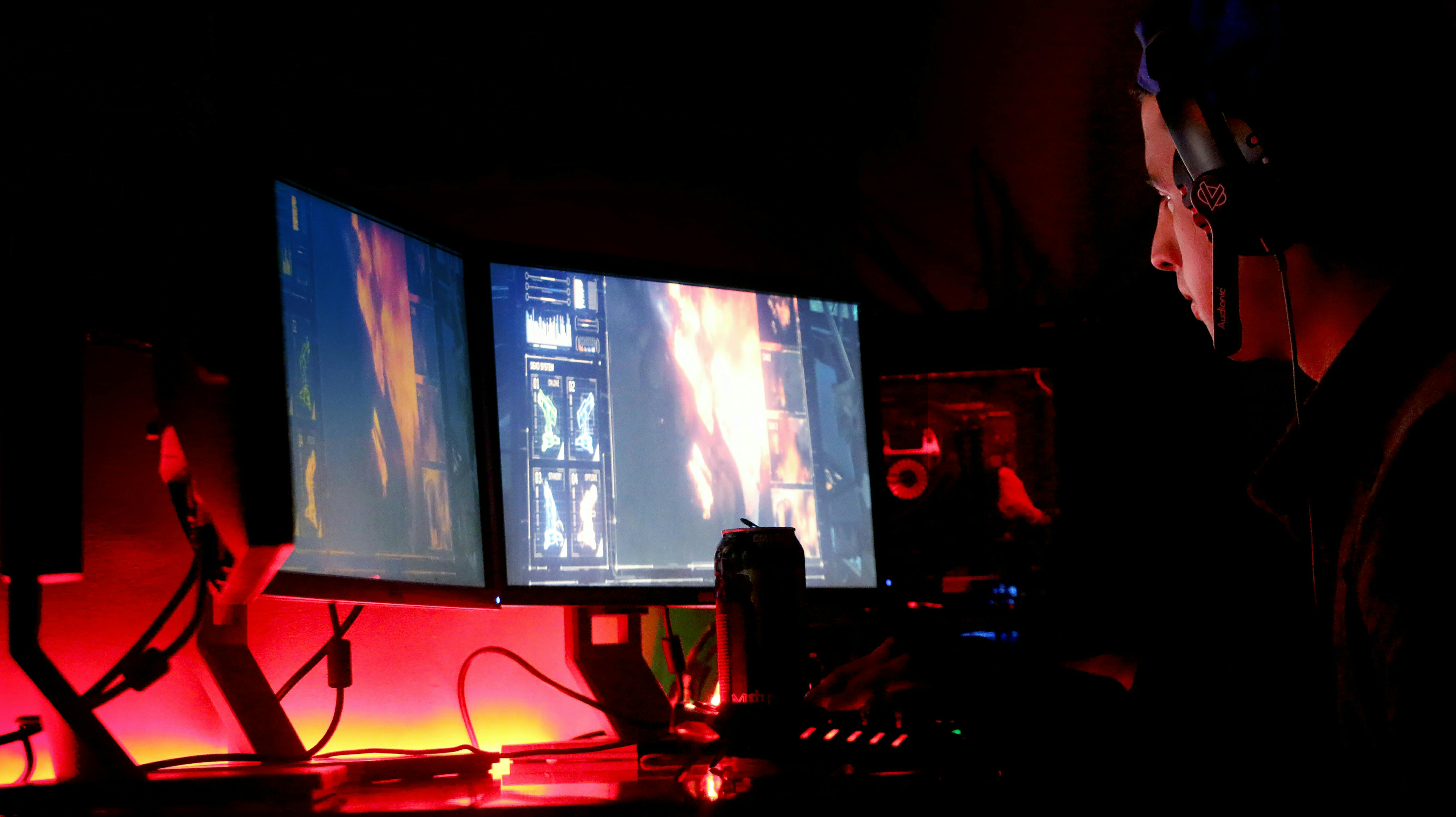 A man intensely focused on multiple computer monitors in a dimly lit room, illustrating high-tech work environment.