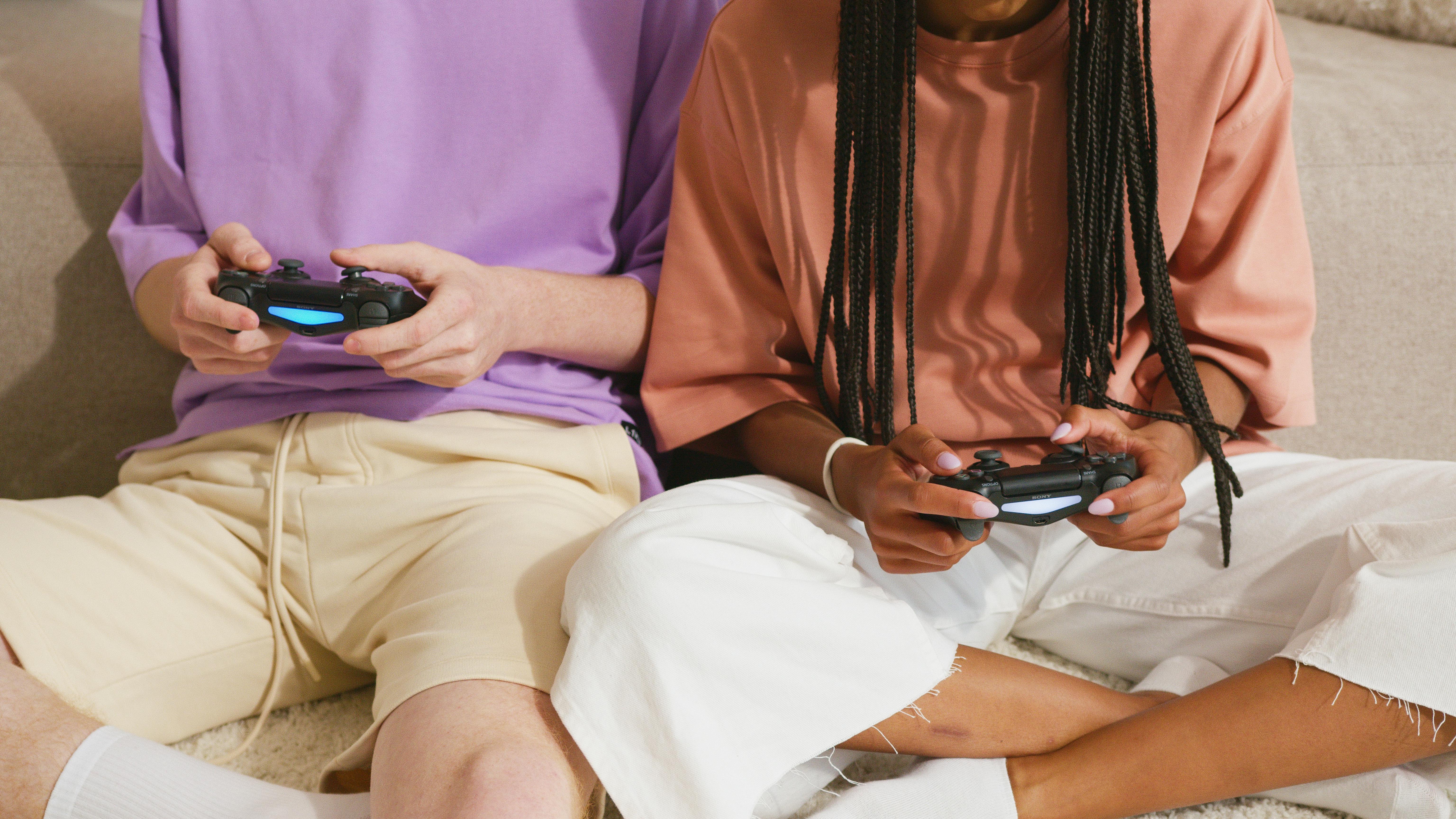 Two young adults sitting indoors, enjoying video games with controllers.